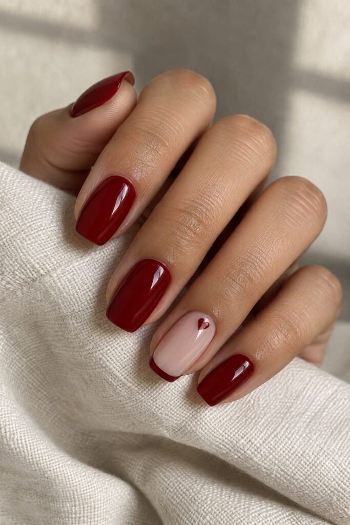 Deep cherry red nails with a tiny heart accent on a milky base