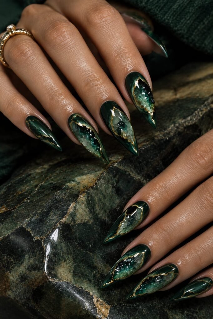 Emerald stiletto nails designed with glossy geode patterns and fine metallic gold veining.