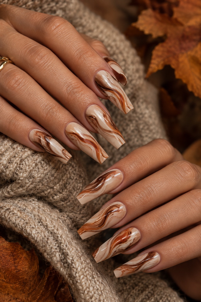 Long coffin nails with creamy beige bases and cinnamon, terracotta, and caramel marble swirls.