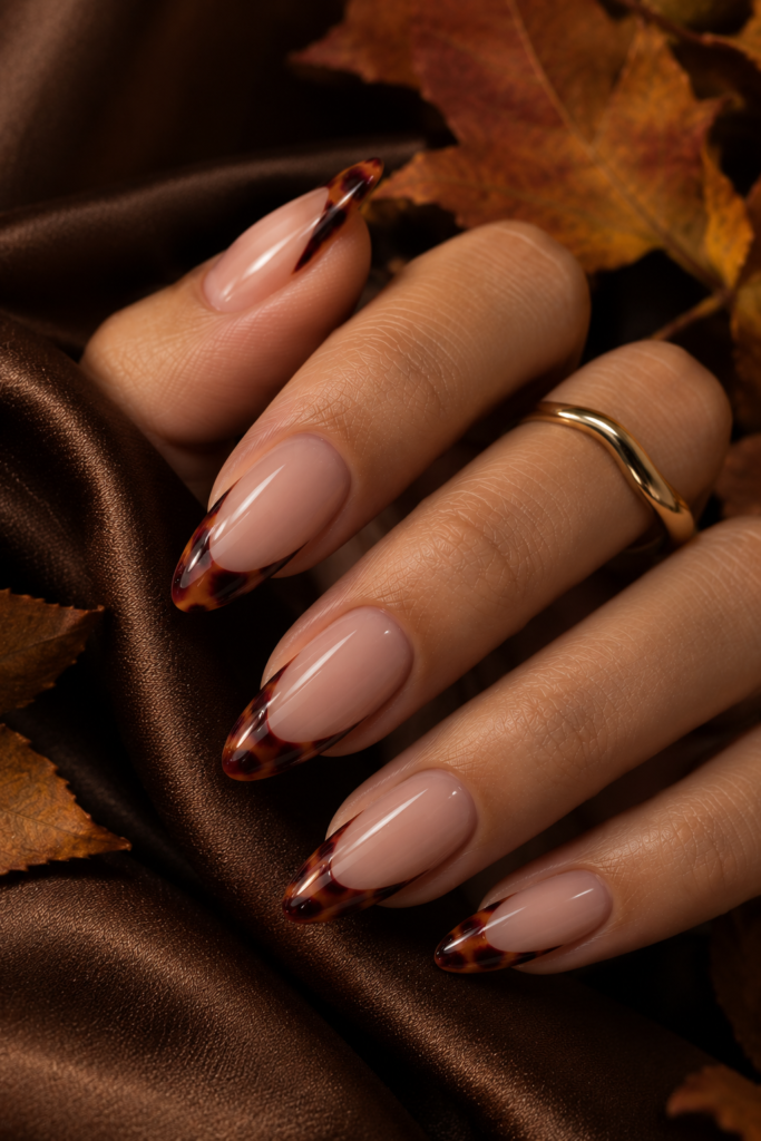 Long oval nails with nude bases and burgundy caramel tortoiseshell French tips.