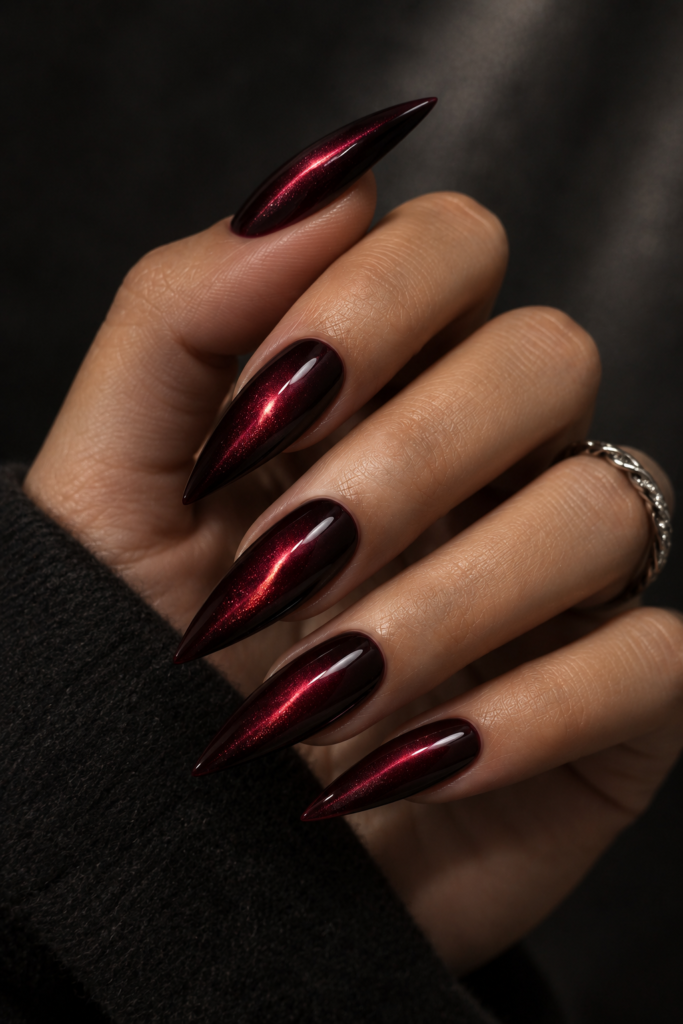 Long stiletto nails in dark black cherry magnetic cat-eye polish with glowing red highlights.