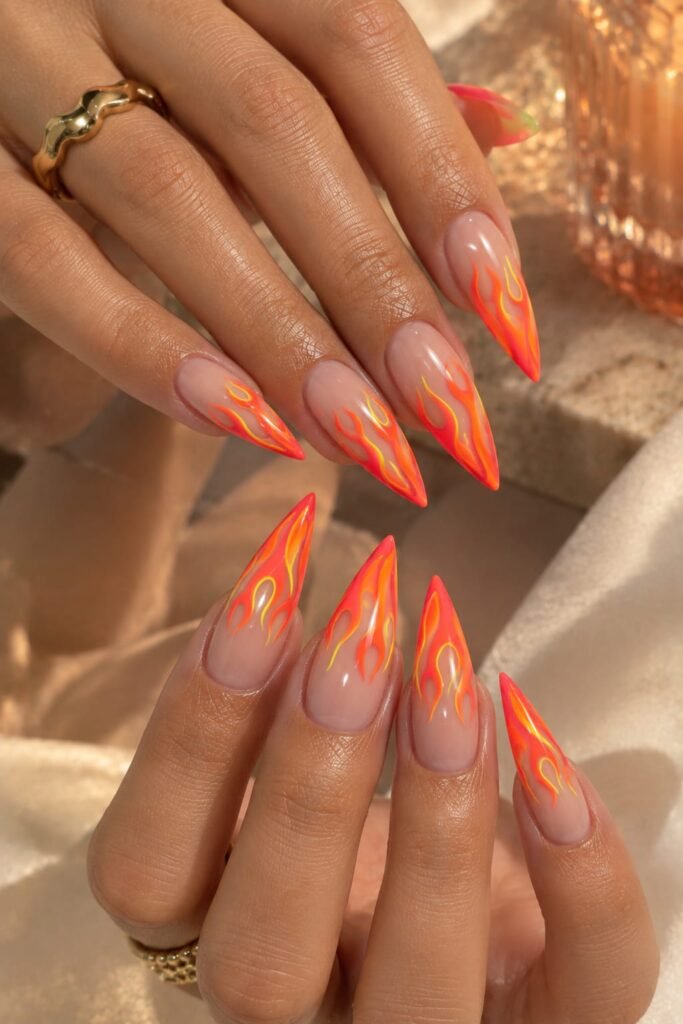 Neon coral flame nails with bright orange and yellow accents on long stiletto nails.