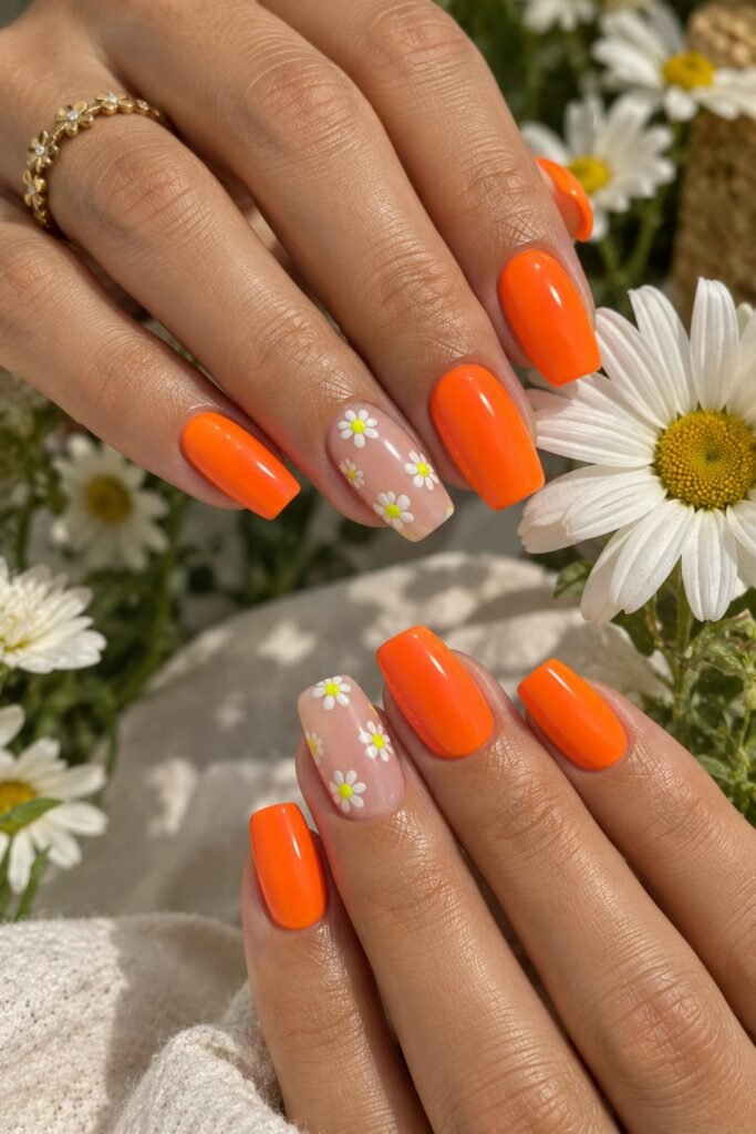 Neon orange daisy nails with white floral accents for a bright summer manicure.