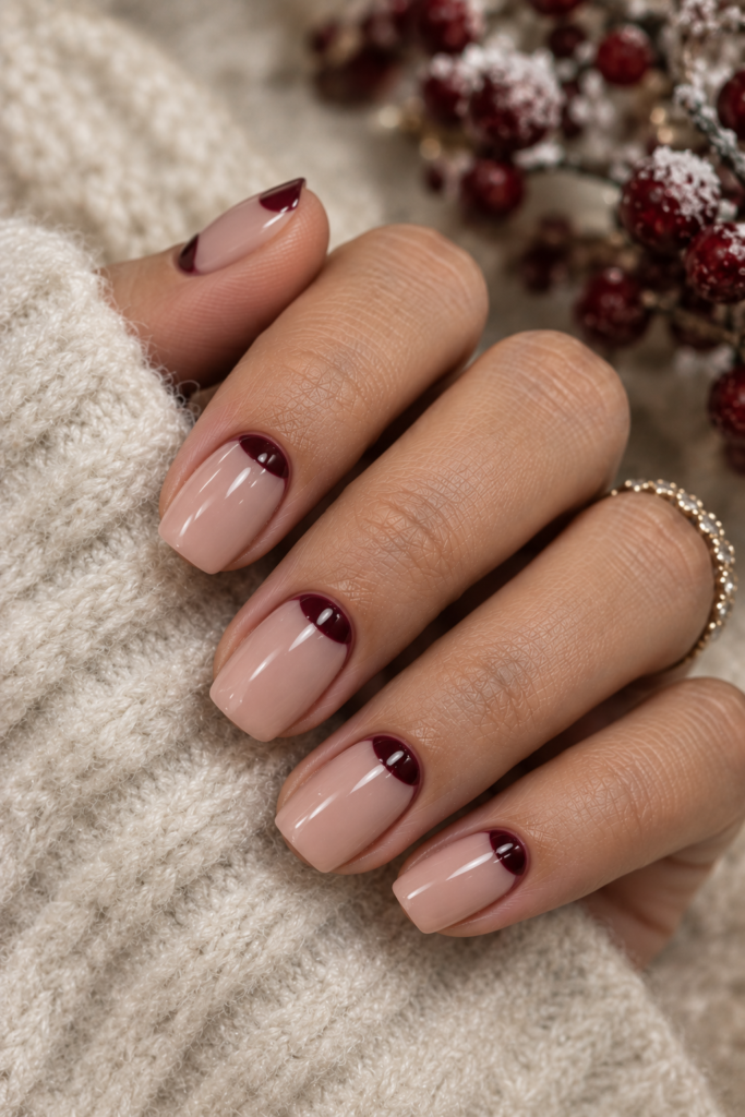 Short square nude nails with deep burgundy half-moon details near the cuticles.