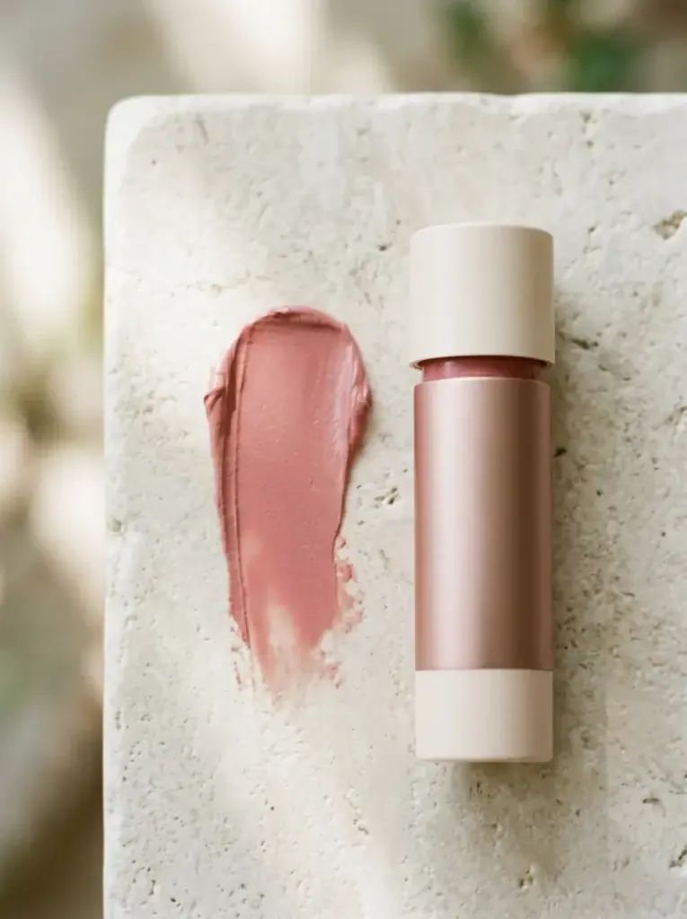 Rosy-pink cream blush stick beside a soft makeup swatch.